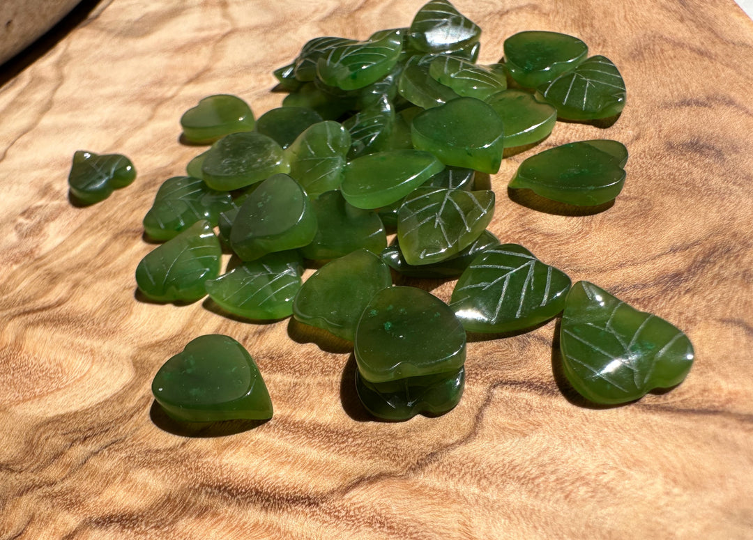 Canadian Jade Leaf beads 9x8mm scattered on a warm wooden surface with white vein patterns