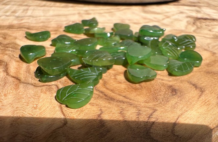 Close up of green jade leaf beads scattered on a wooden surface.