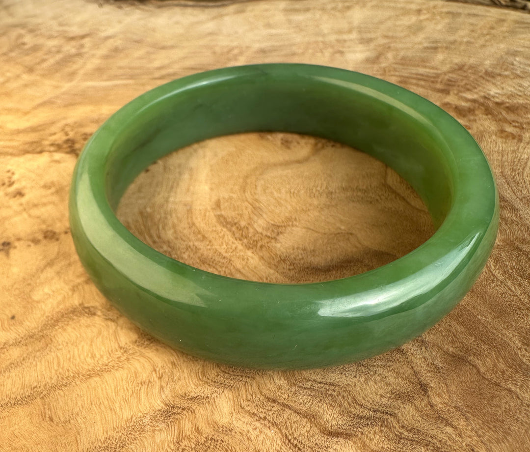 Siberian Bangle in green jade with a thick circular form resting on a wood surface.