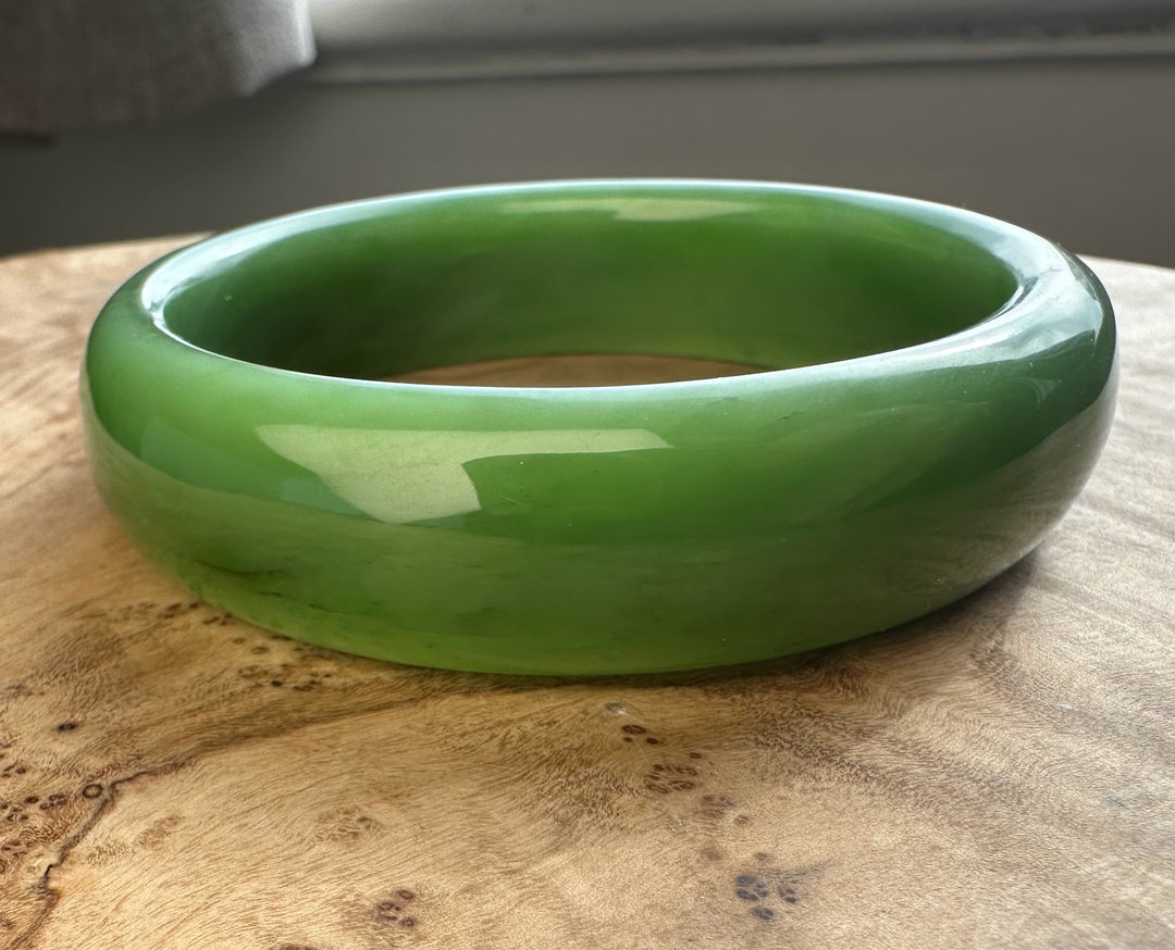 Close up of glossy green jade bangle with a smooth rounded exterior on a wooden surface.