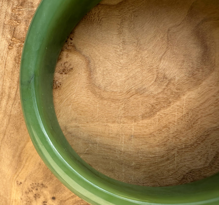 Edge view of green jade Siberian Bangle highlighting its thick rounded profile on wood.
