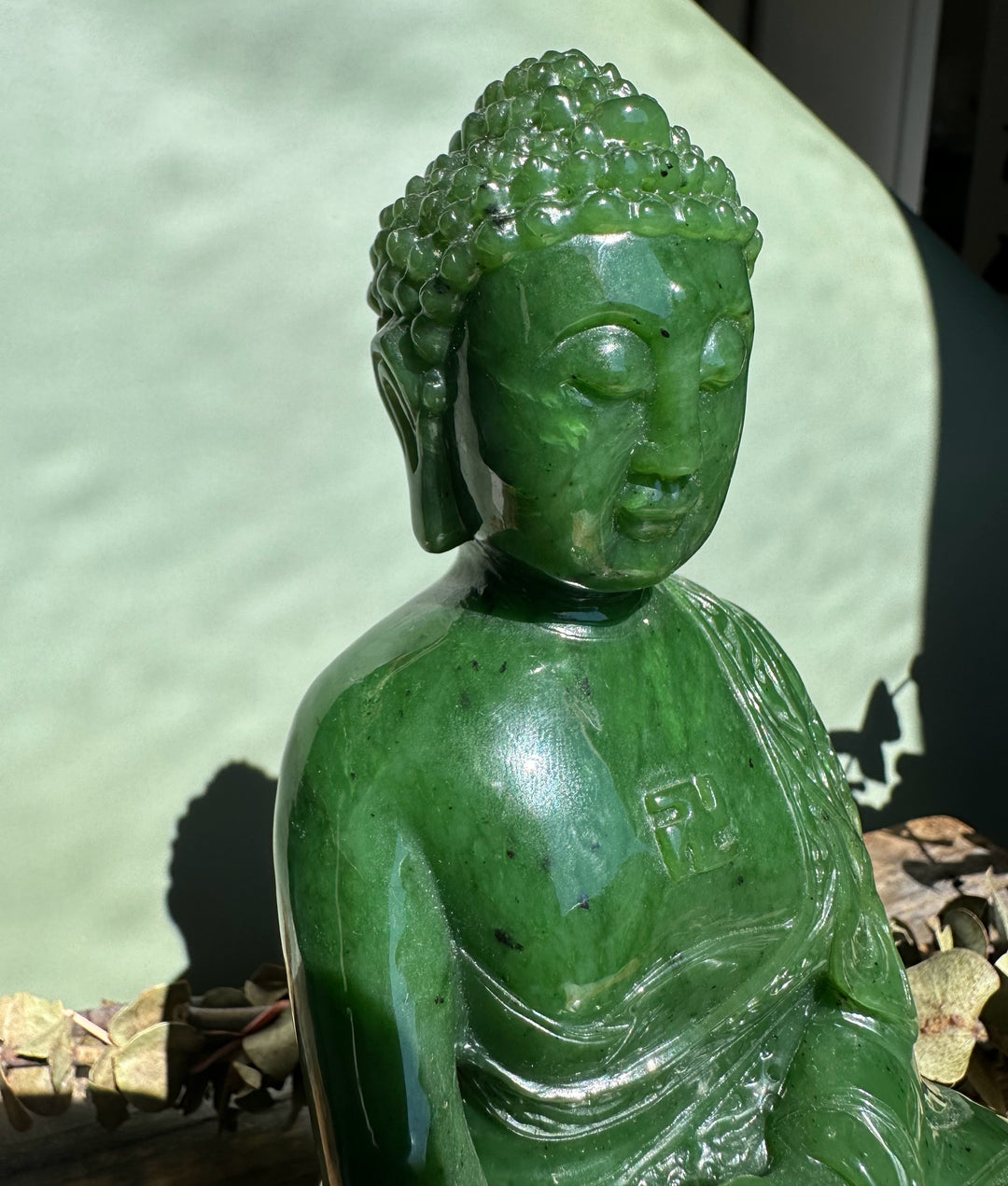 Close up of green nephrite jade Shakyamuni Buddha head and torso with detailed curls and calm expression