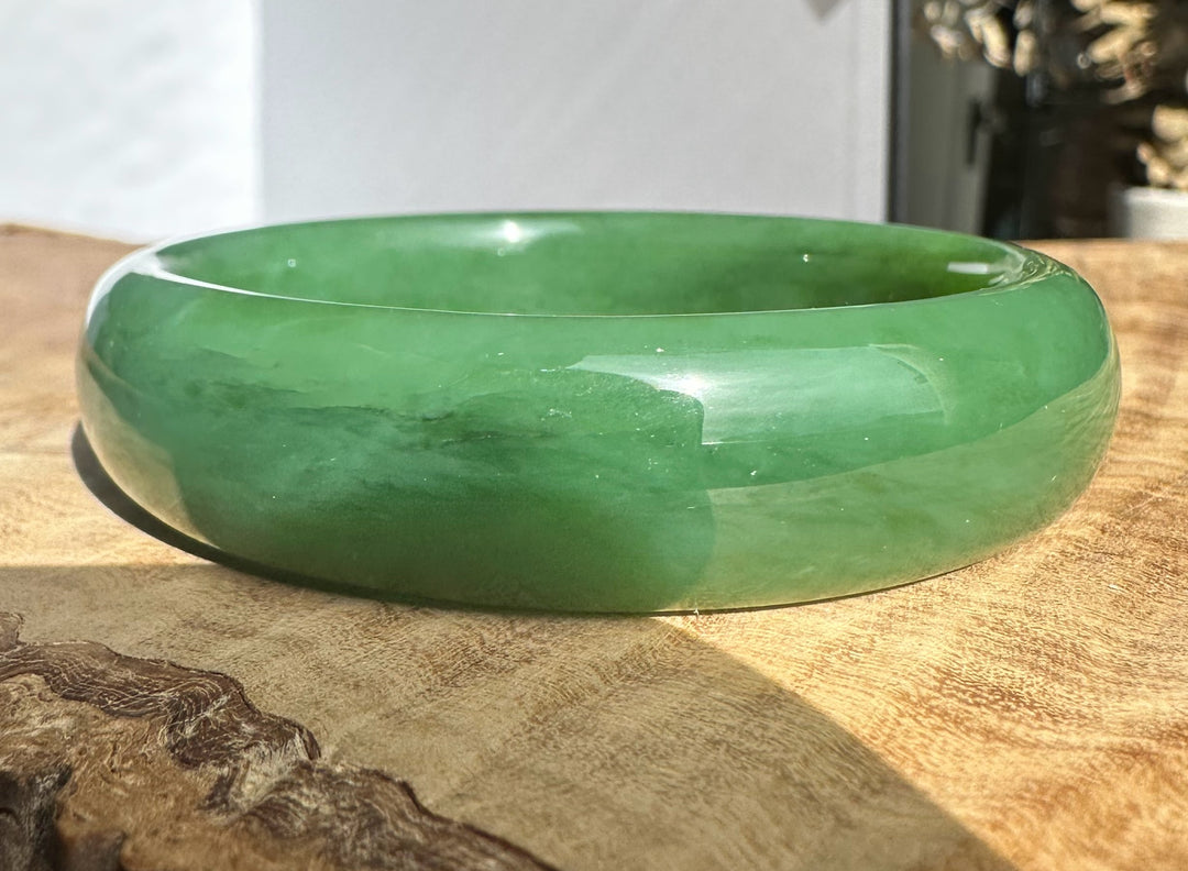 Siberian jade bangle in emerald green on a wooden surface.