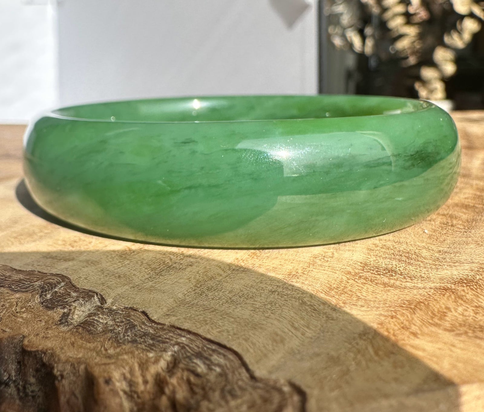 Siberian Bangle in green jade with a smooth polished surface resting on a wooden textured backdrop