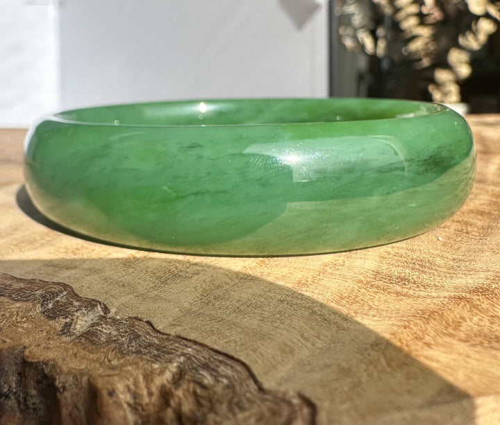 Siberian Bangle in green jade with a smooth polished surface resting on a wooden textured backdrop