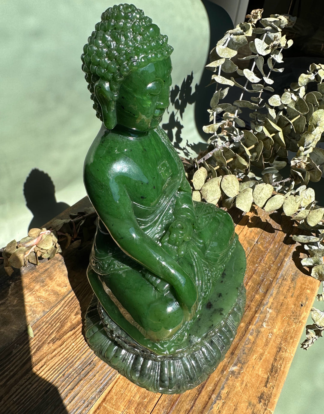 Green nephrite jade Shakyamuni Buddha viewed from the side, seated in meditation on a carved base