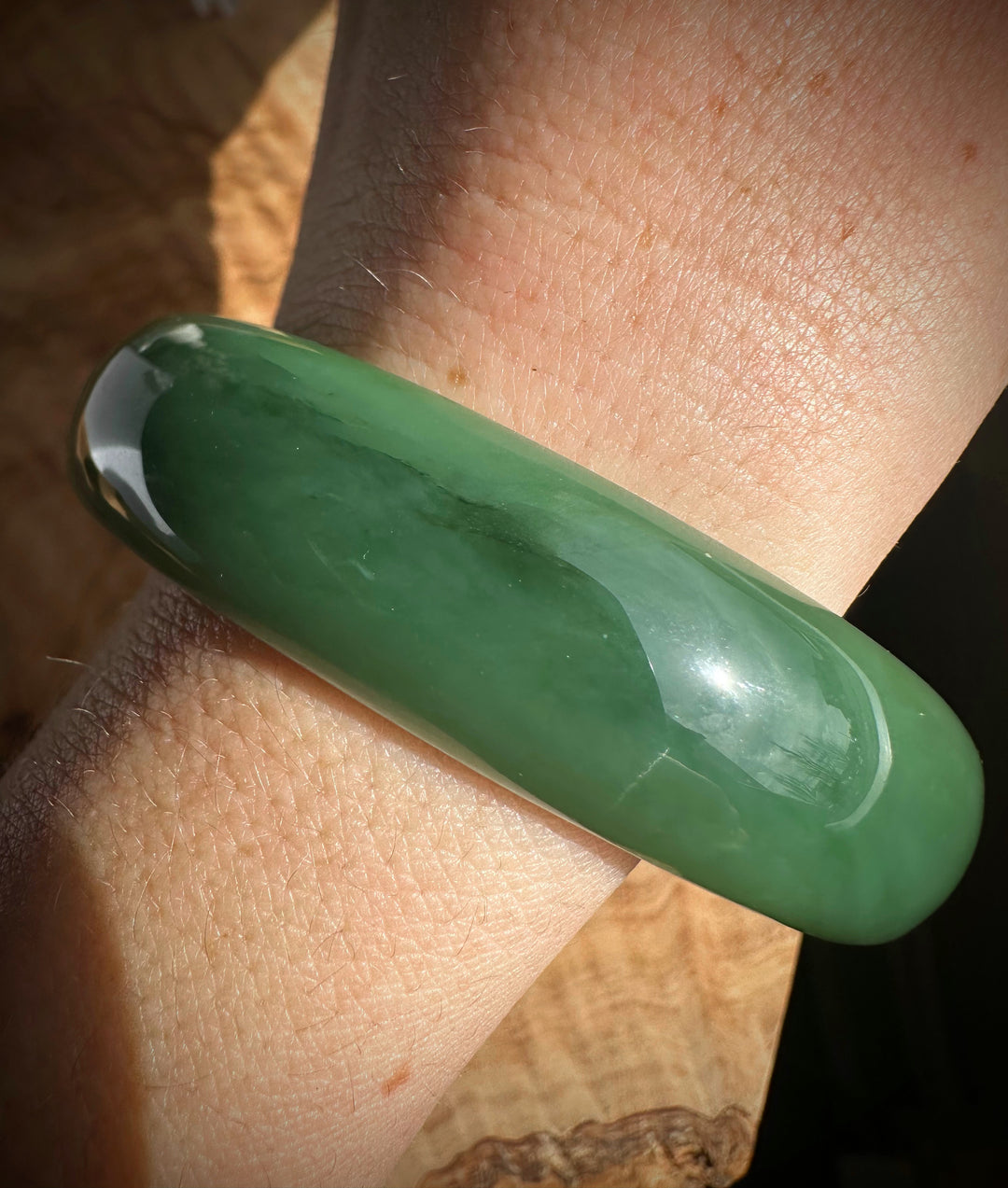 Wrist wearing a thick polished green jade bangle in sunlight.