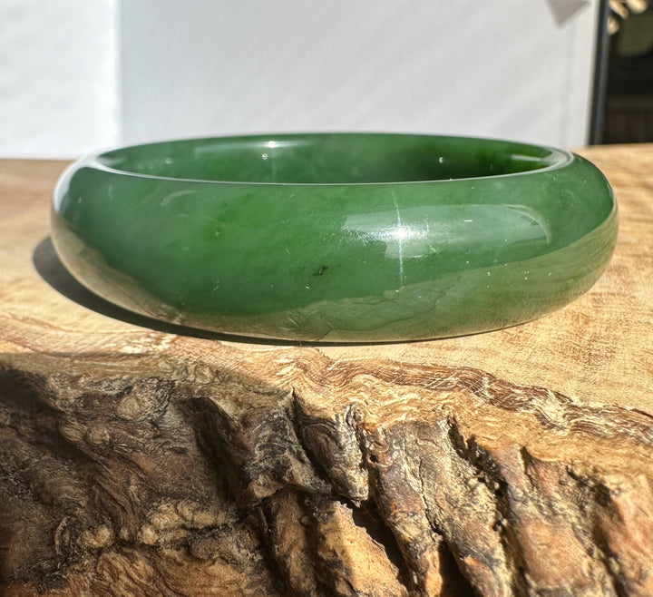 Canadian Jade Bangle 54.5 x 15mm in polished green jade resting on a rustic wood surface