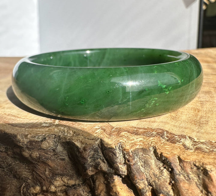 Canadian Jade Bangle 54.5 x 15mm polished green jade bracelet resting on a textured wood surface