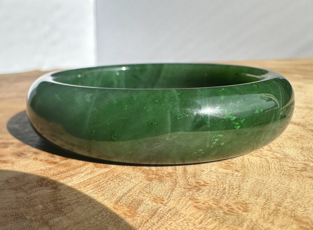 Side view of the Canadian Jade Bangle highlighting deep green color and natural patterns on wood