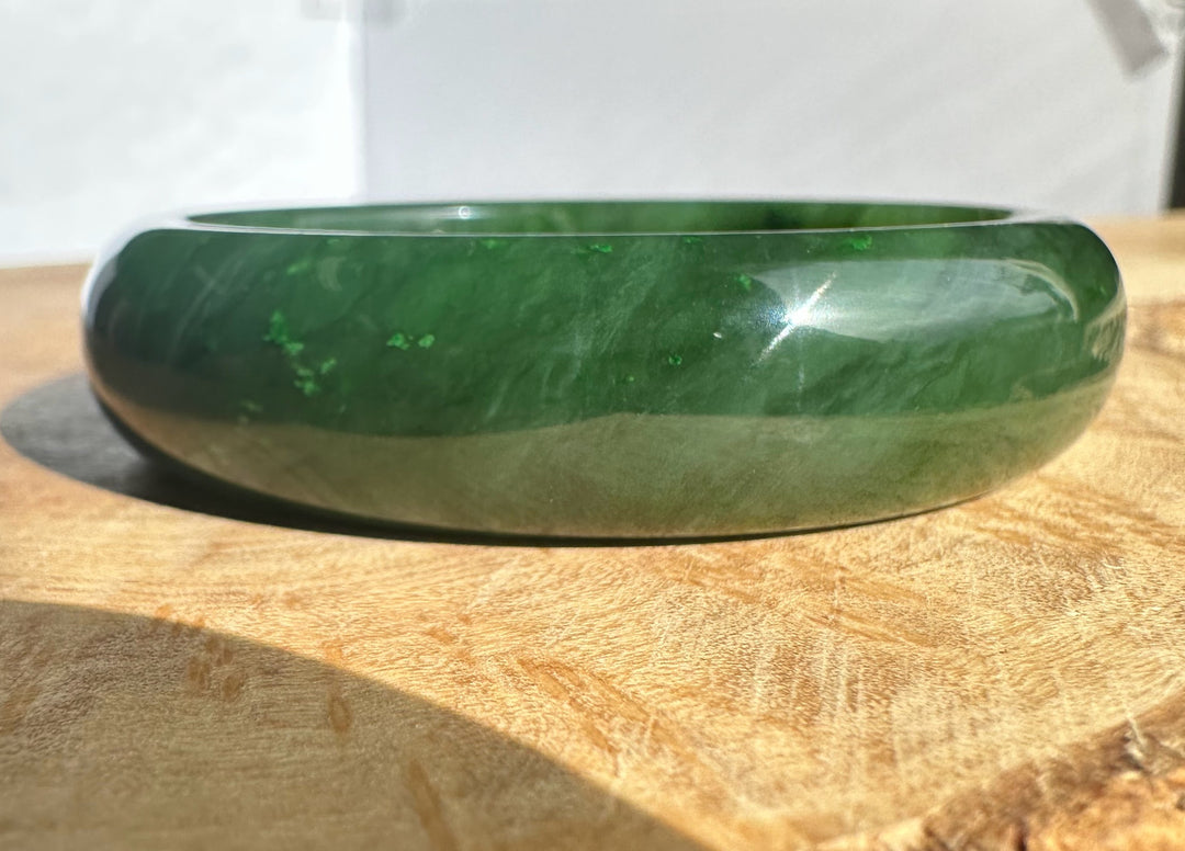 Canadian Jade Bangle in deep green with a glossy finish resting on a wooden surface