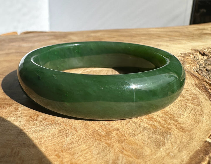 Side view of a glossy jade bangle with rich green color on a wooden surface