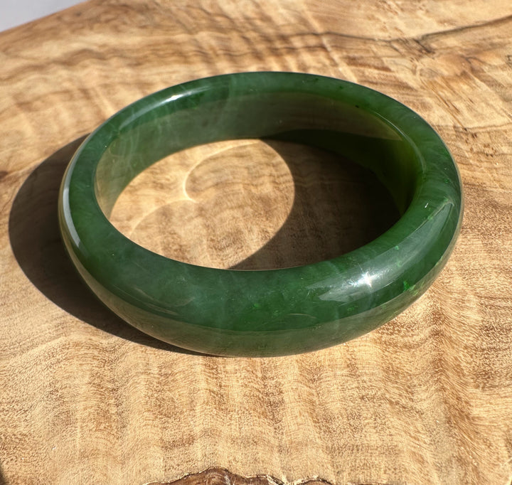 Canadian Jade Bangle in dark emerald green with a polished glossy finish on a wood surface
