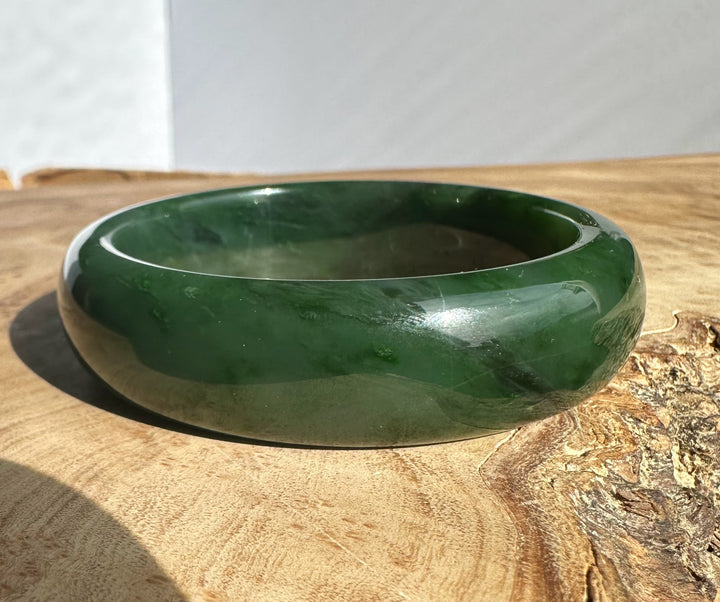 Glossy green jade bangle with rounded edges resting on a wooden surface