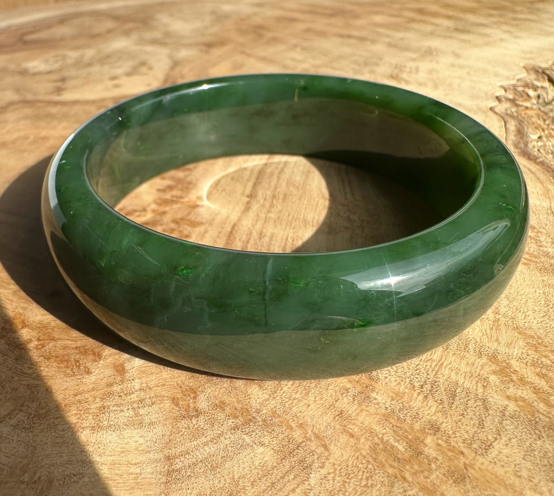 Canadian Jade Bangle 56 x 17mm, dark green polished bracelet resting on a wooden surface