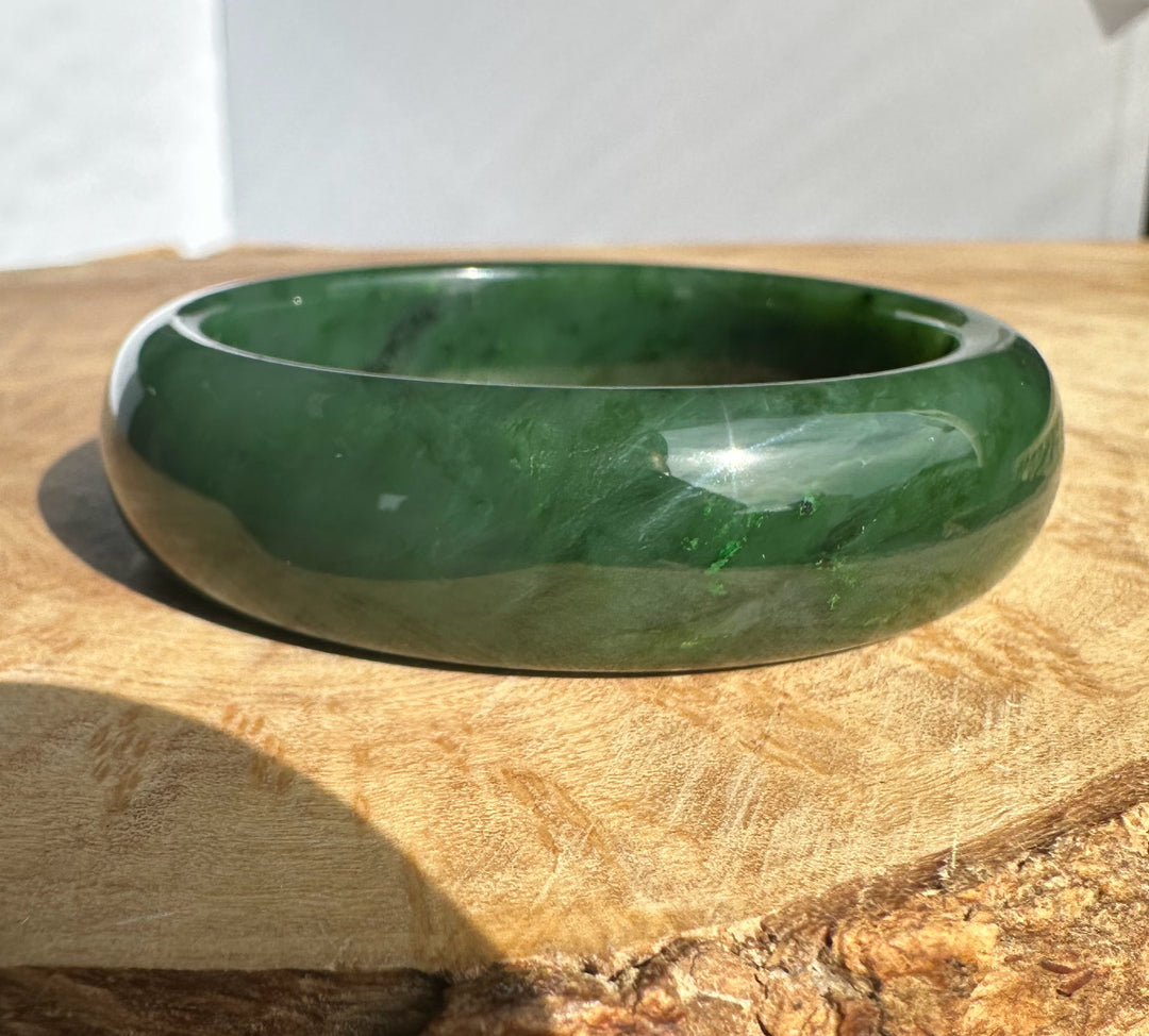 Canadian Jade Bangle 56 x 17mm, rich green jade bracelet photographed from the side on wood