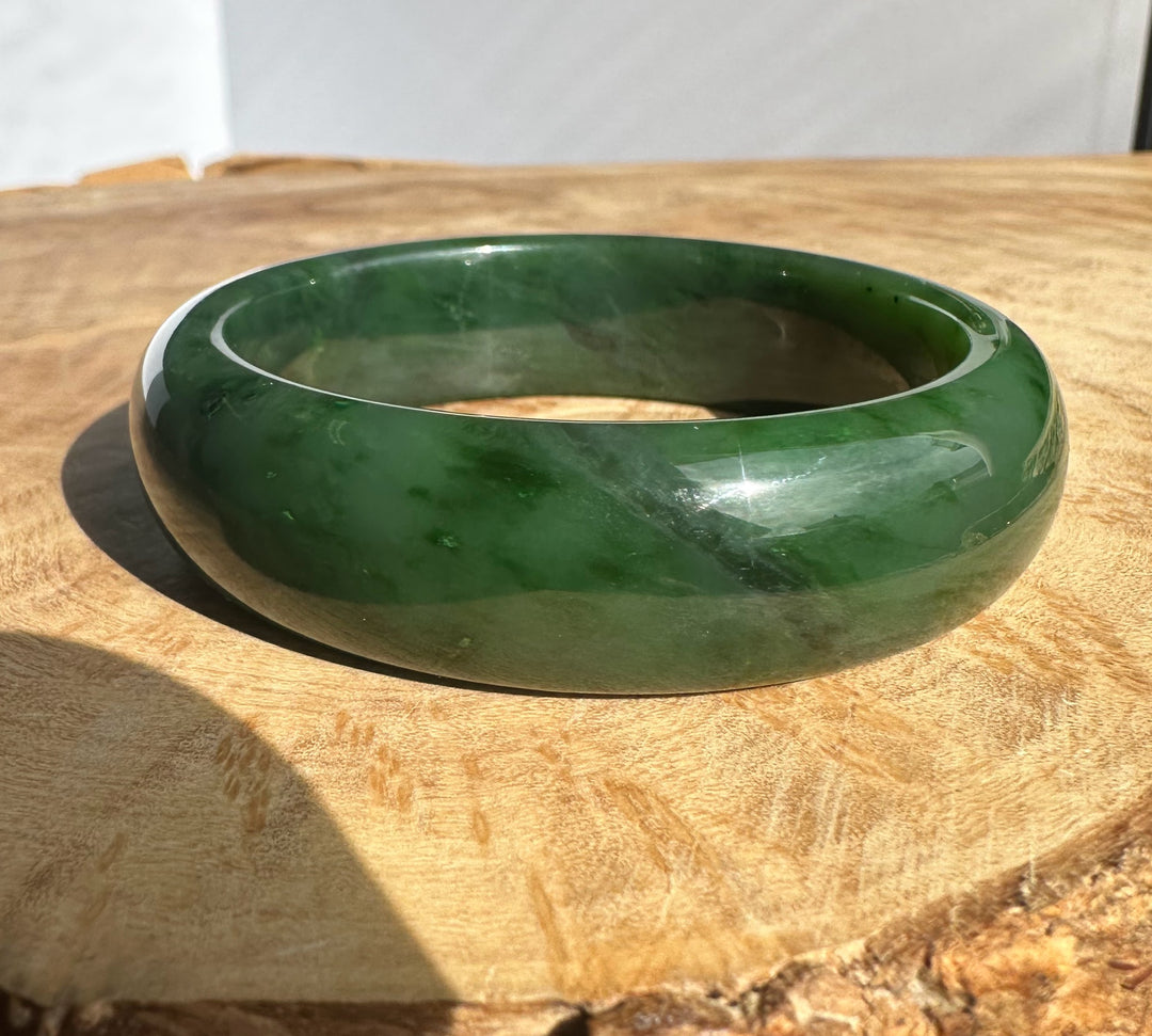 Canadian jade bangle with a glossy green finish resting on a wooden surface