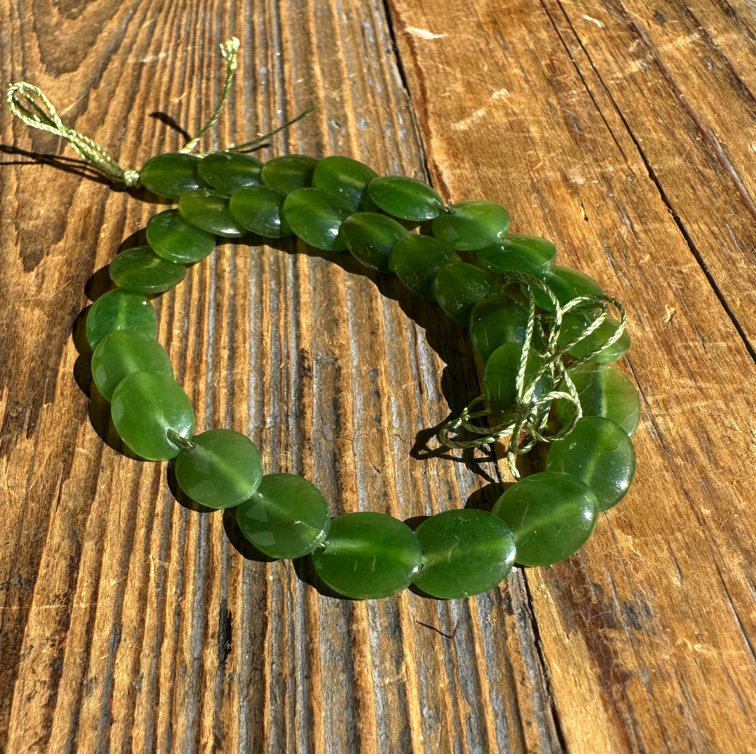 Two strands of green jade lentil beads tied with a cord bow on a wooden surface
