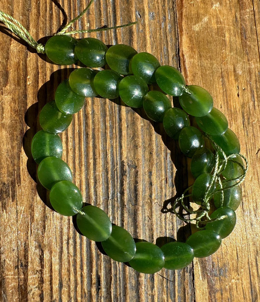 Long strand of green jade lentil beads on a weathered wooden surface.