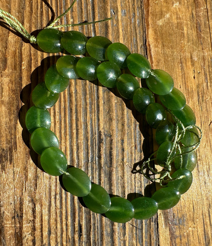 Long strand of green jade lentil beads on a weathered wooden surface.
