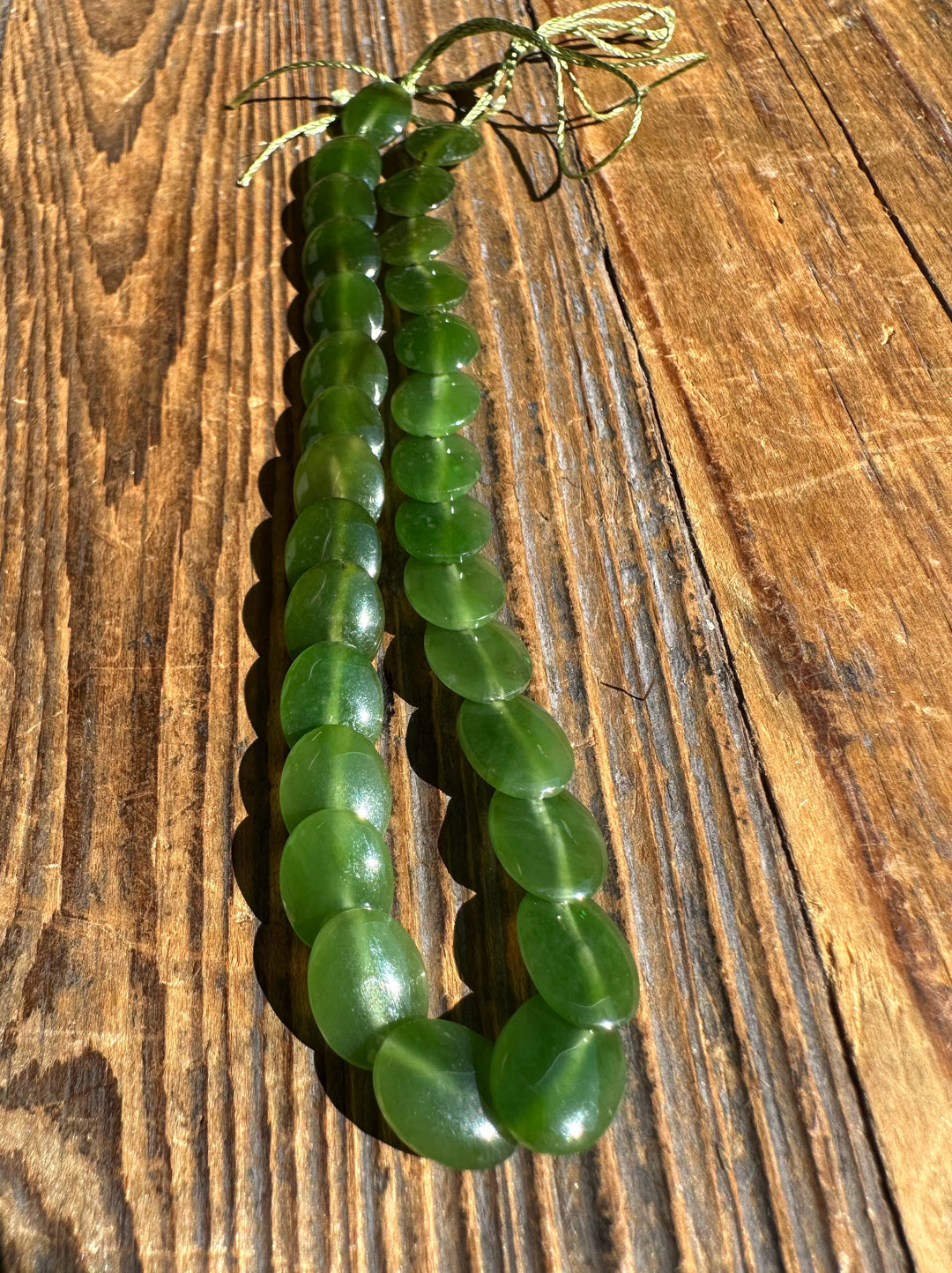 Single strand of green jade lentil beads laid on wood with a knotted cord at the end