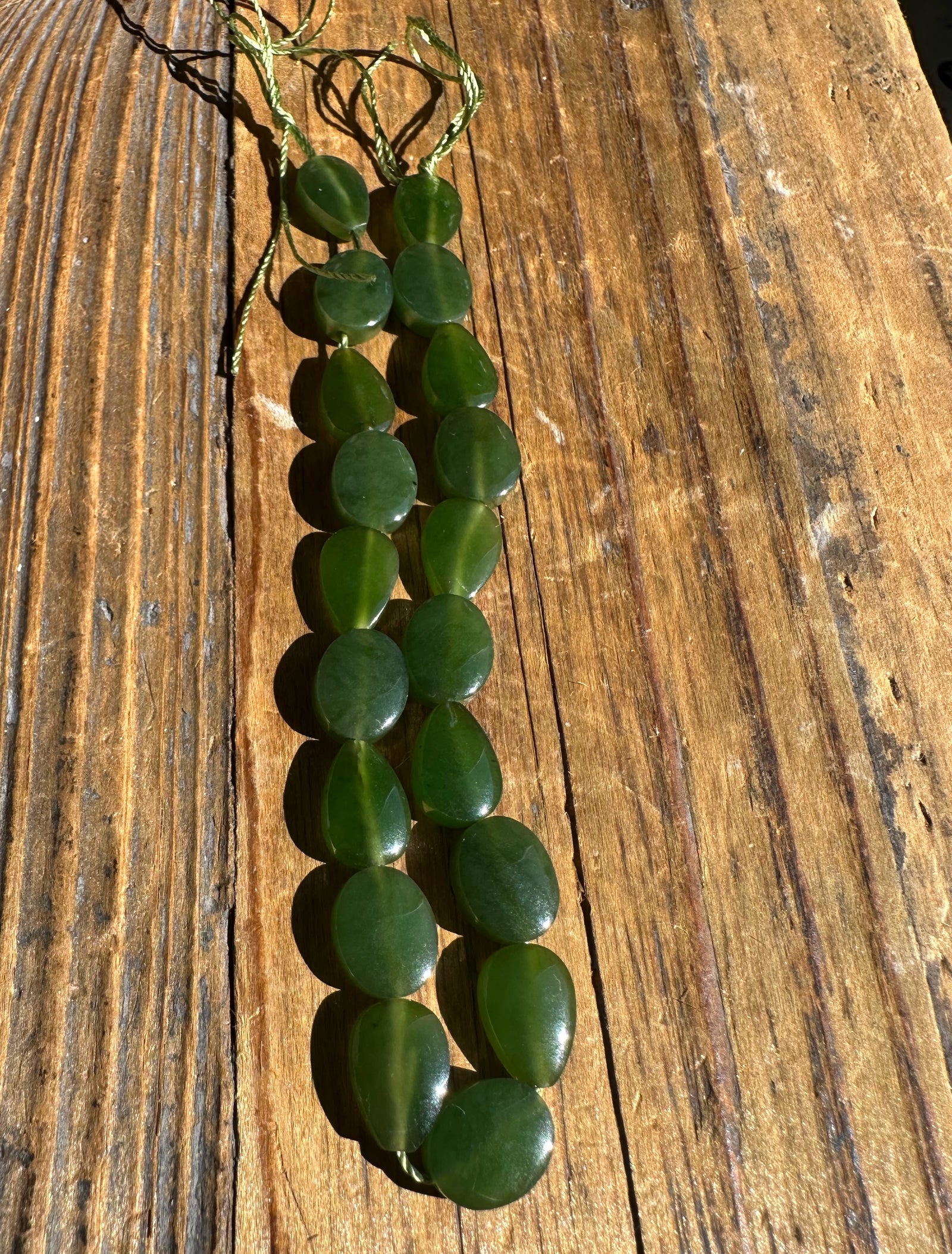 Two strands of dark green jade beads for a bracelet resting on a weathered wooden surface.