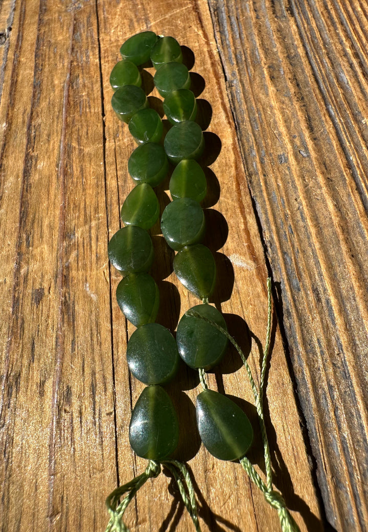 Close-up of two strands of circular jade beads with green cord on a weathered wooden surface.