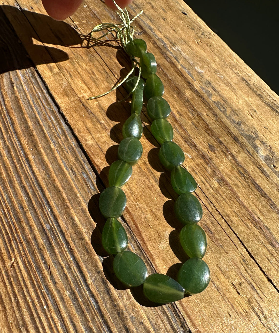 Two strands of flat round Canadian jade beads tied with a green cord on a weathered wooden surface.