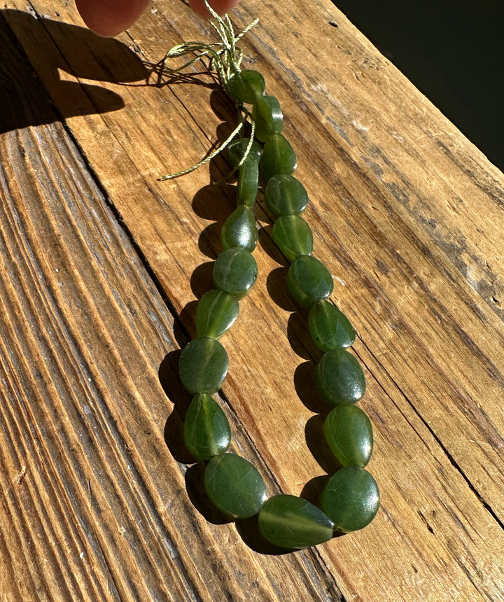 Two strands of flat round Canadian jade beads tied with a green cord on a weathered wooden surface.