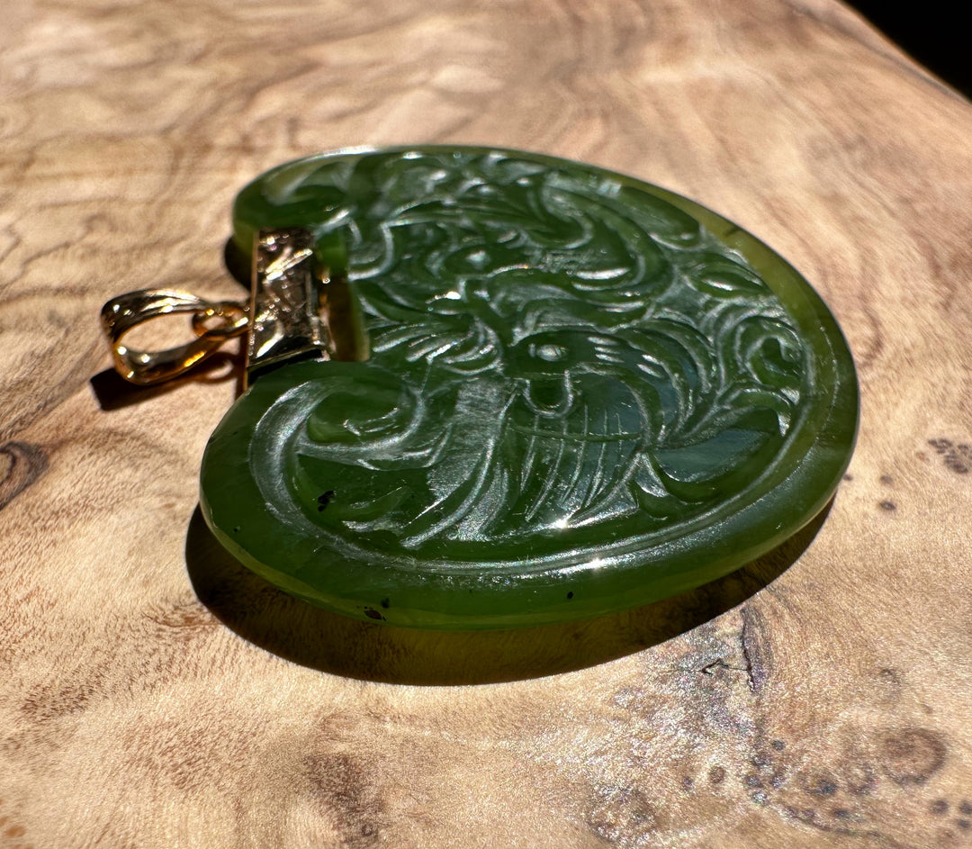 Vintage green jade birds pendant with intricate scrollwork and a gold bail on a wooden surface