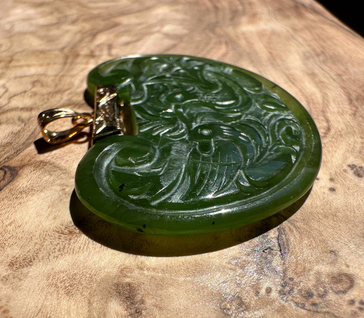 Vintage green jade birds pendant with intricate scrollwork and a gold bail on a wooden surface