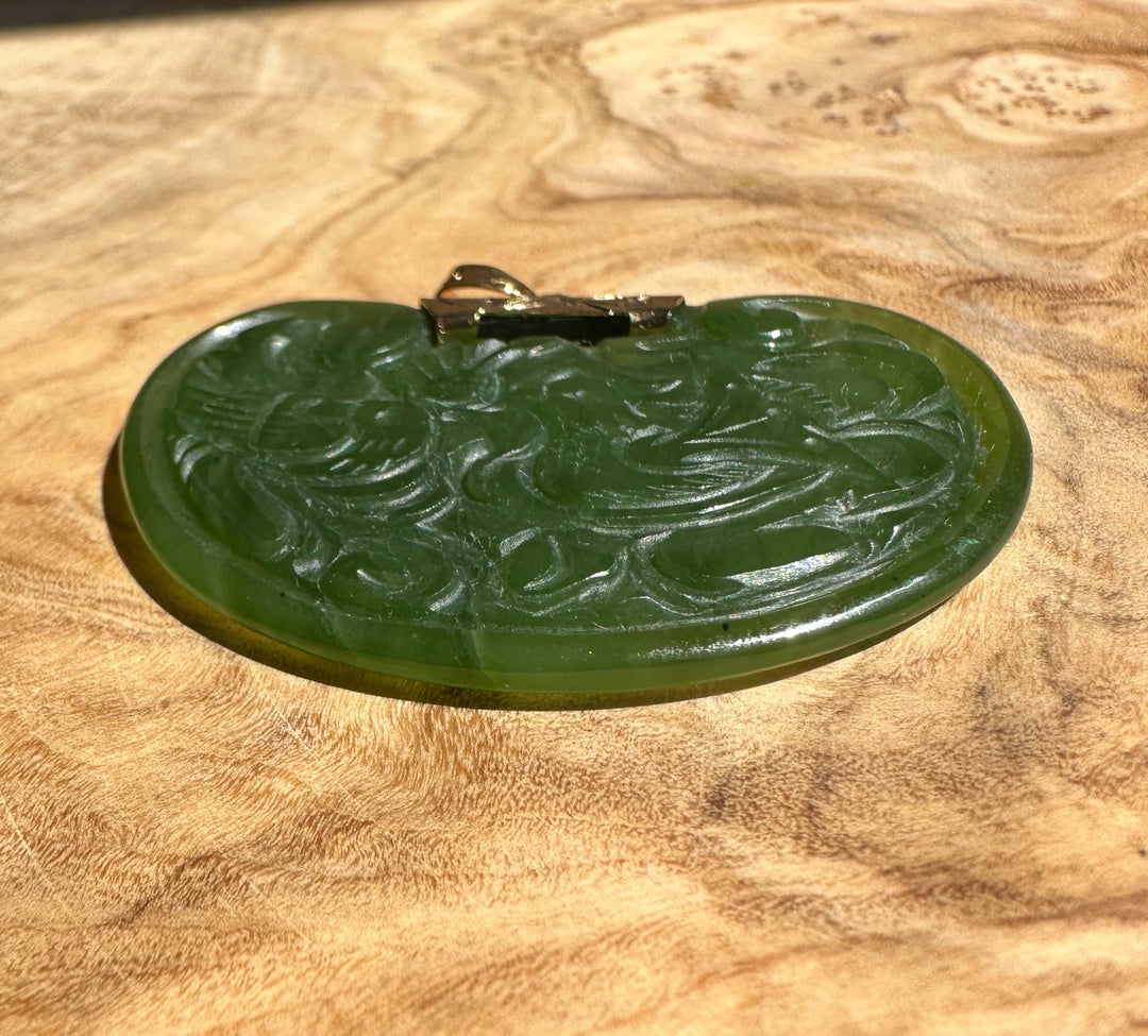 Oval green jade pendant with detailed bird and swirl carving and a gold bail