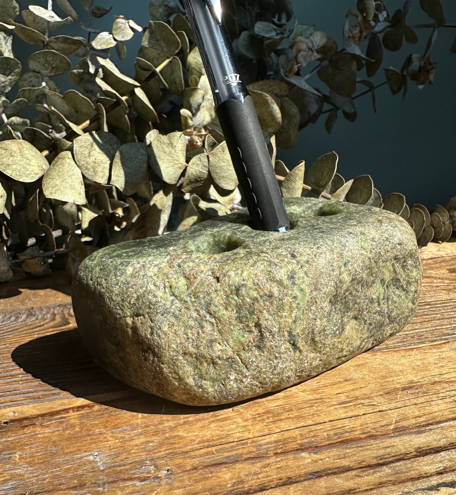 Rough jade pen holder with a metal pen inserted into one of its top holes.