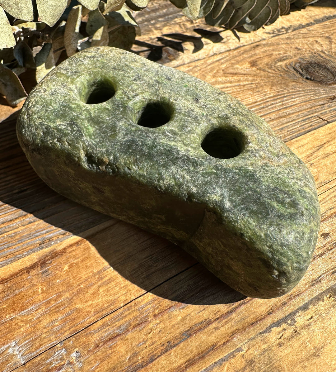 Close up of rough jade pen holder showing three top holes on a green mottled stone.