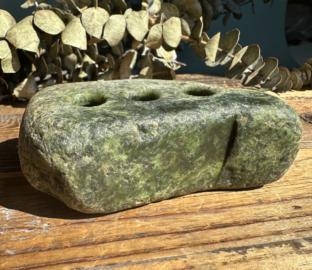 Rough jade pen holder with three holes on top resting on a wooden surface.