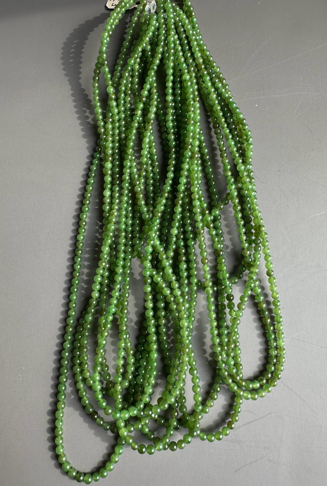Multiple strands of 3.5mm unstrung A grade Canadian nephrite jade beads on a grey surface