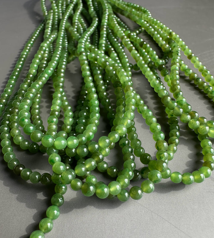 Close up of small round green nephrite jade beads arranged in curved strands on a grey surface