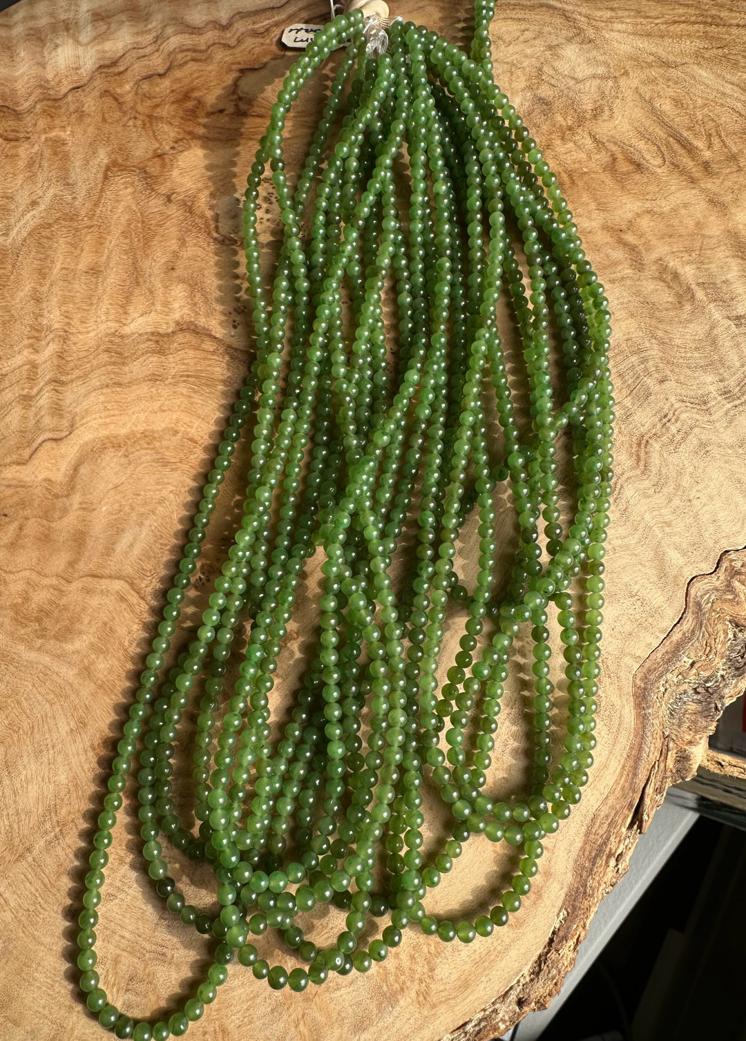 Bundle of 3.5mm green nephrite jade bead strands on a wooden background