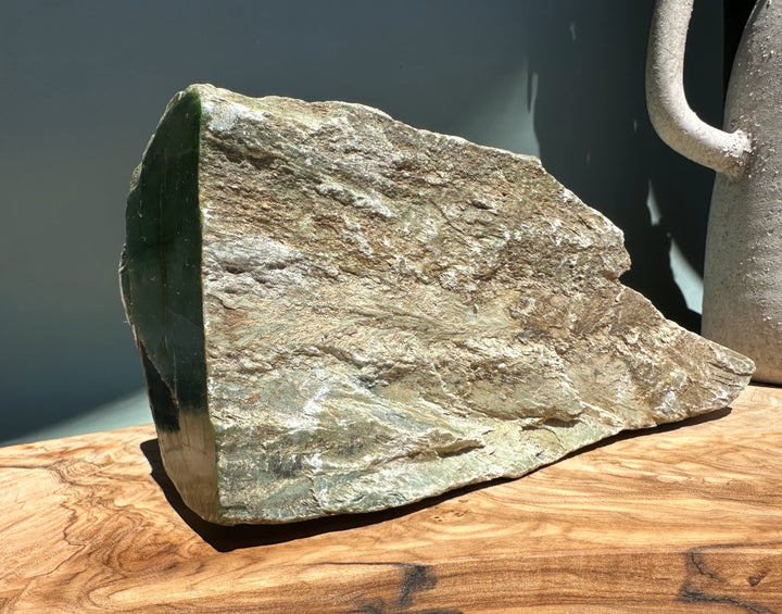 Siberian nephrite rough block with a dark green face and brown weathered crust on a wooden surface.