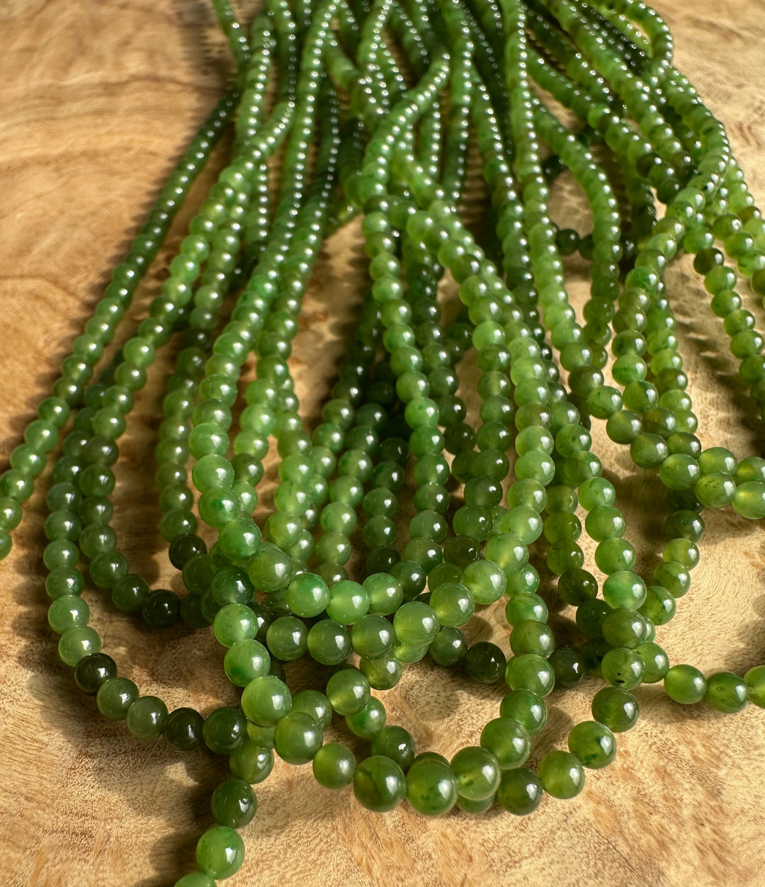 Close up of 3.5mm green nephrite jade beads arranged in strands on wood