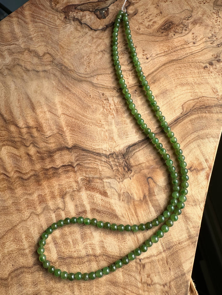 Unstrung green nephrite jade beads arranged on a rustic wood surface.