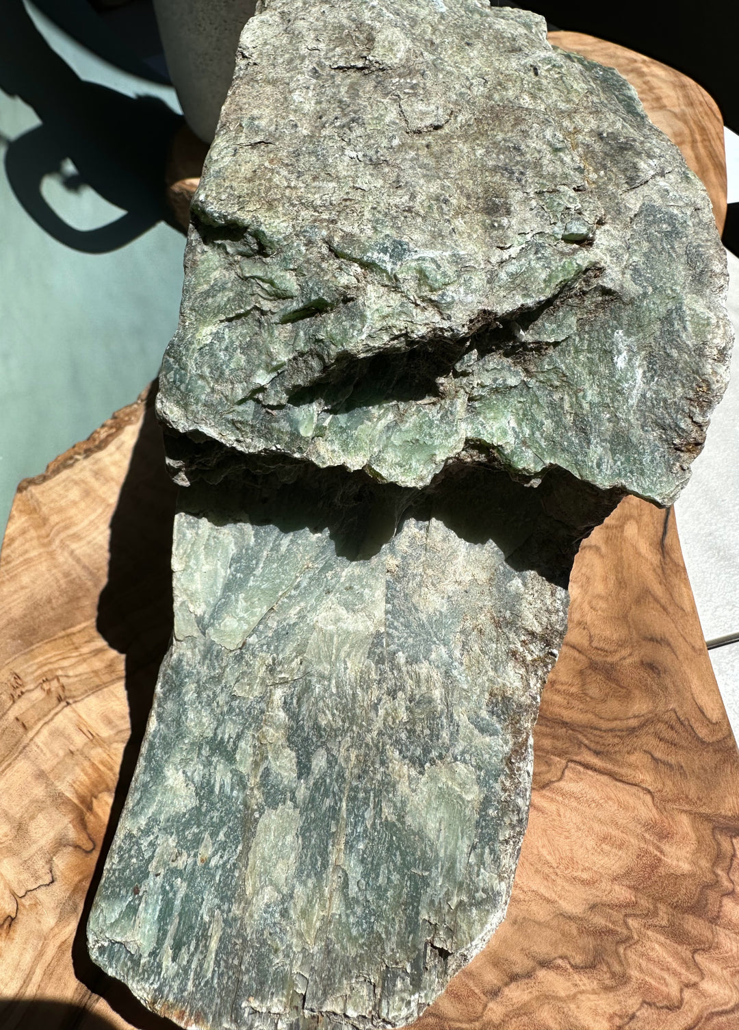 Rough Siberian nephrite jade rock with green gray surface on a wooden base