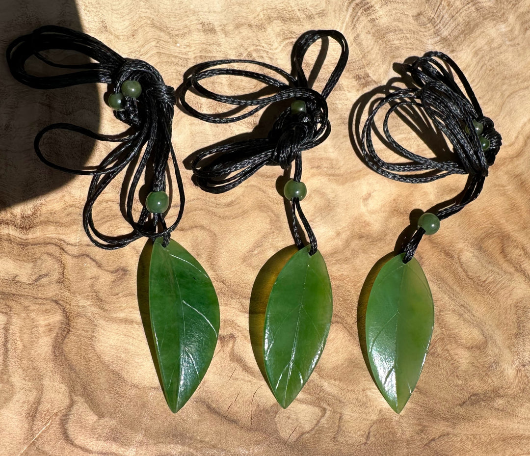 Three green leaf pendants on black cords with small green beads, laid out on a wooden surface.