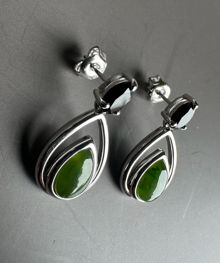 Silver earrings with green nephrite jade teardrops set in layered teardrop frames on a grey surface