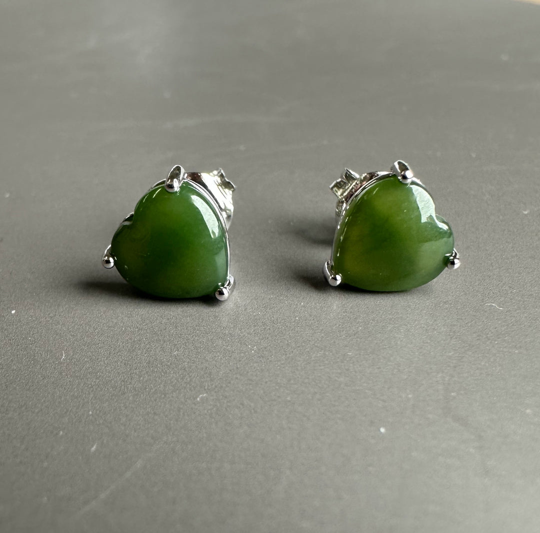 Pair of green jade heart earrings in silver settings on a gray surface.