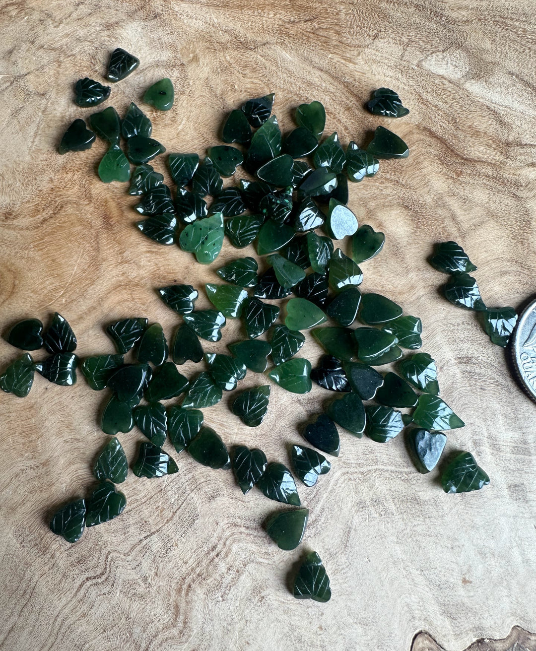 Scattered green jade leaf beads on a wooden surface