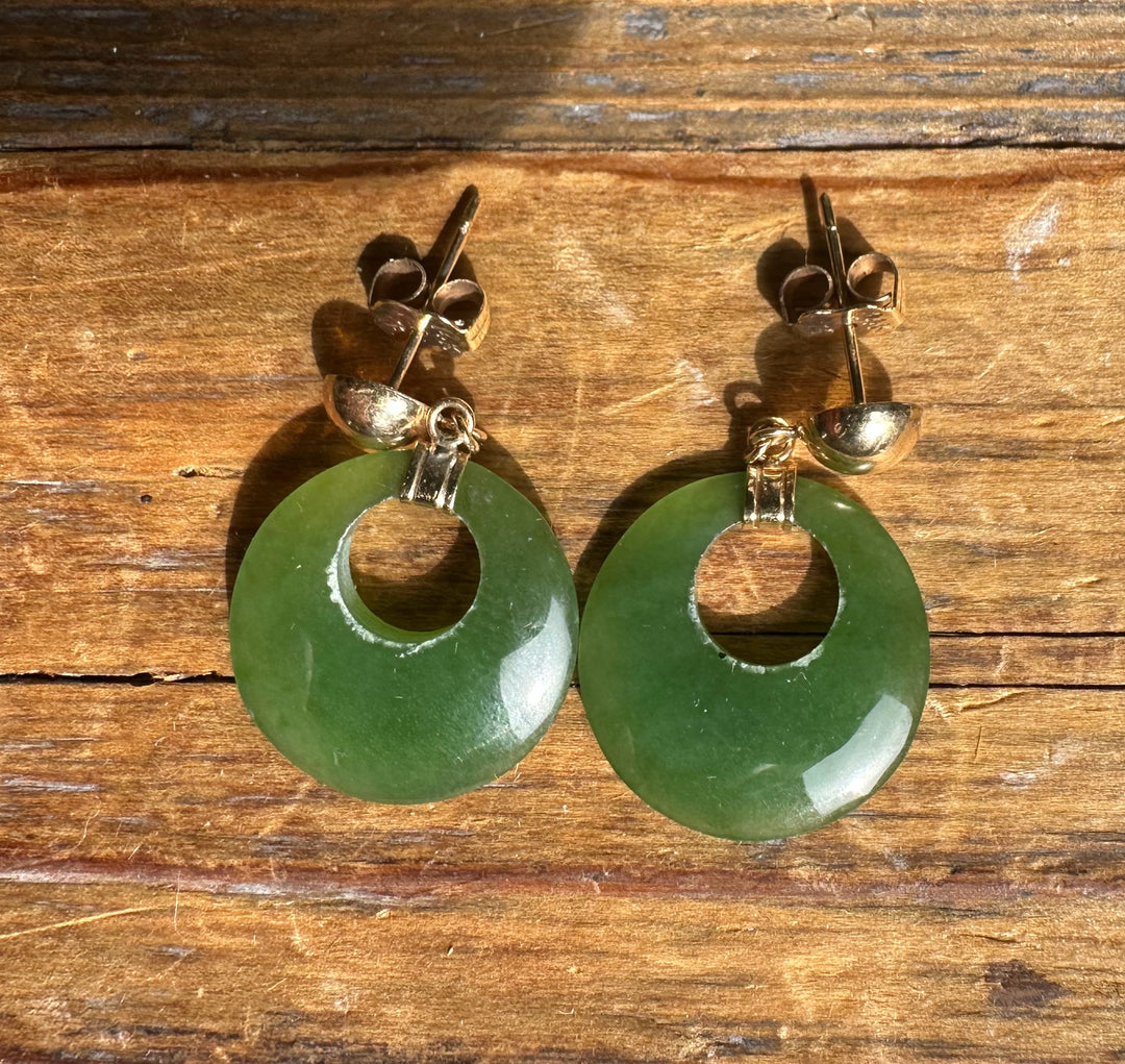Pair of Vintage Jade Round Drop Earrings with green donut discs and gold-tone hardware resting on wood.