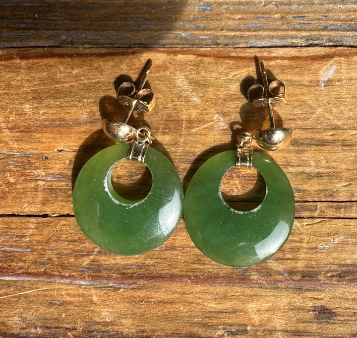 Pair of Vintage Jade Round Drop Earrings with green donut discs and gold-tone hardware resting on wood.