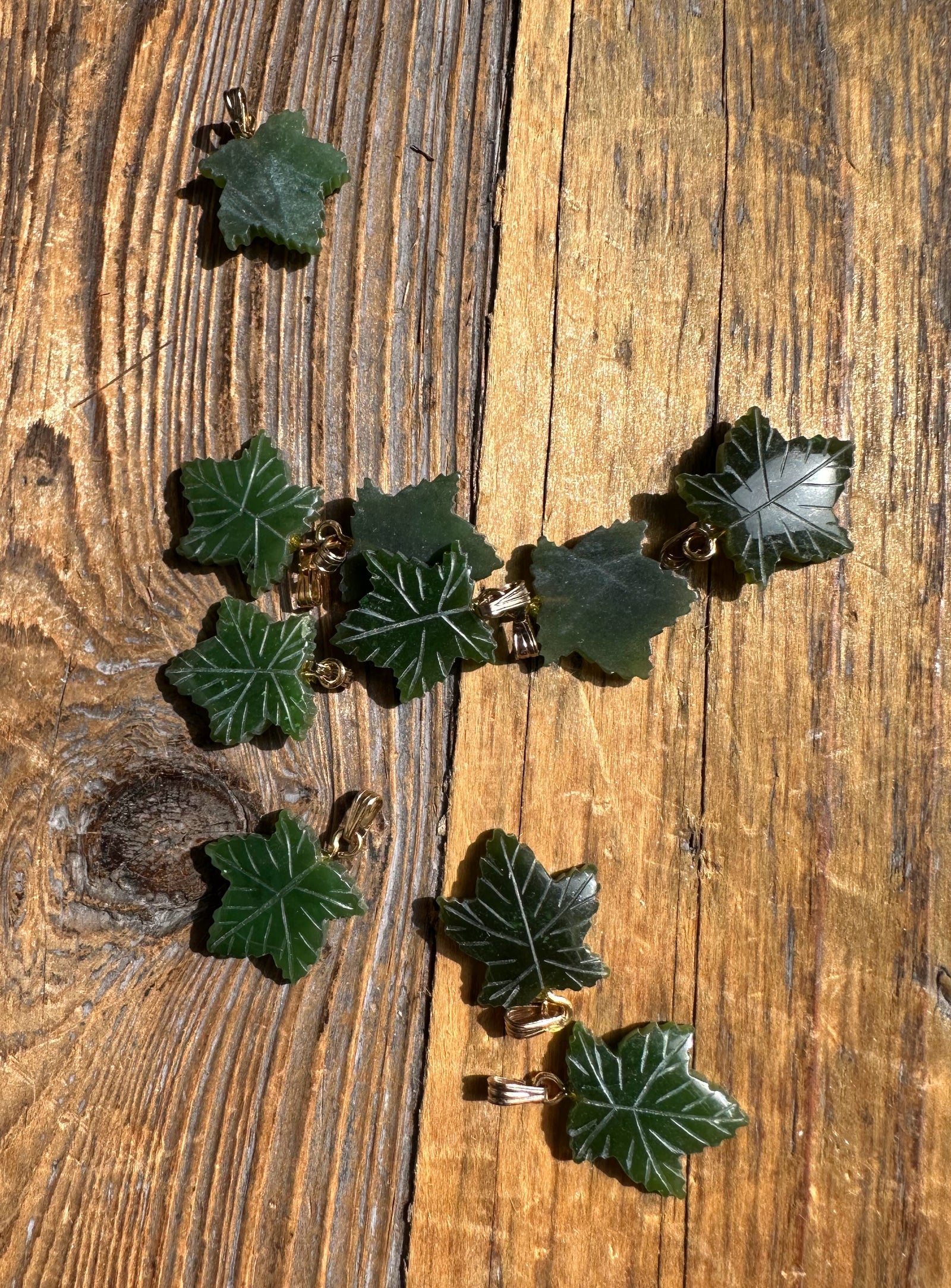 Green maple leaf pendants with gold findings scattered on a rustic wooden surface.
