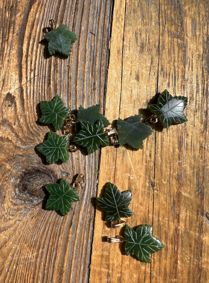 Green maple leaf pendants with gold findings scattered on a rustic wooden surface.